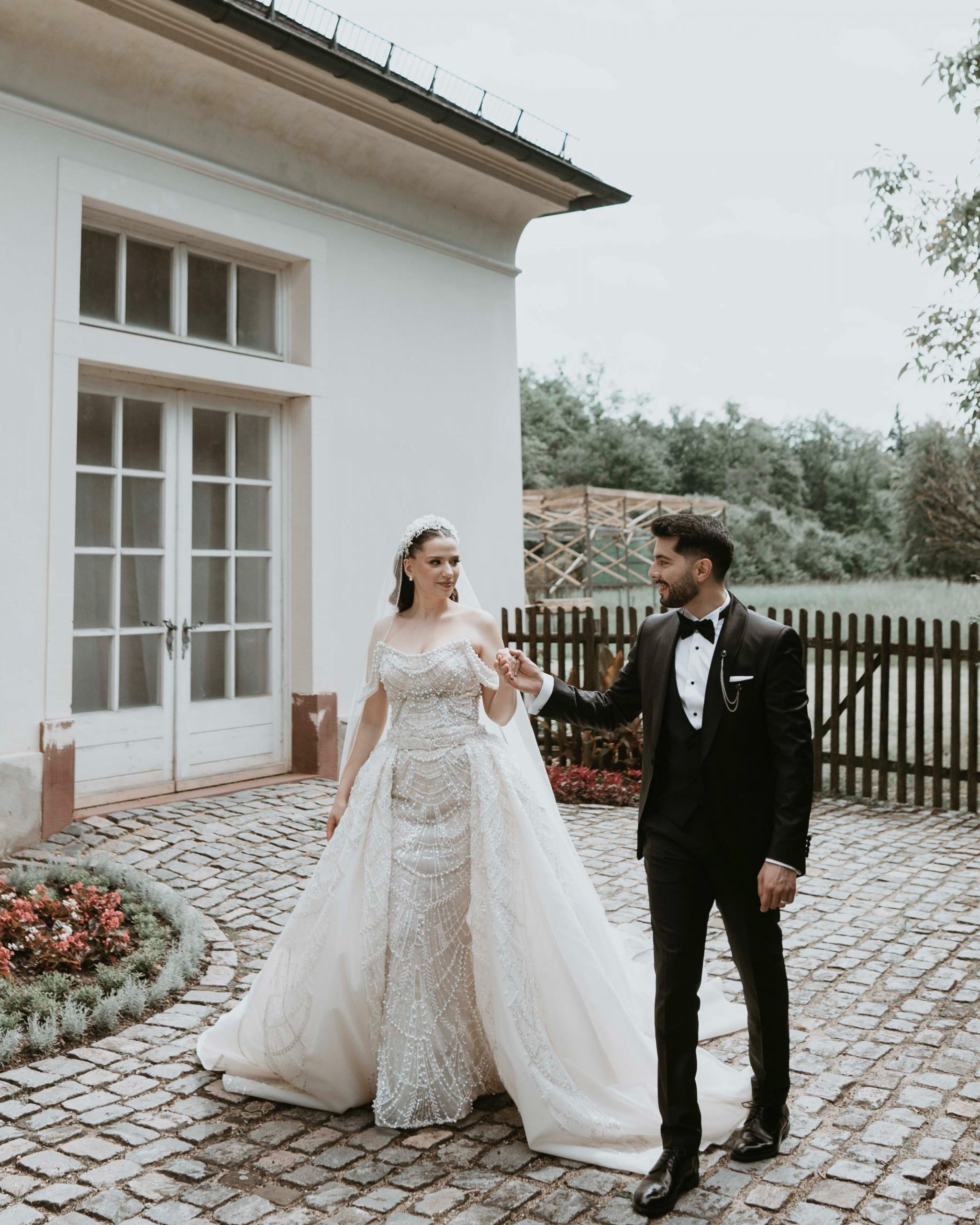 Ein Brautpaar steht im Freien, elegant gekleidet in Abendmode. Die beiden blicken sich an und lächeln einander glücklich an.