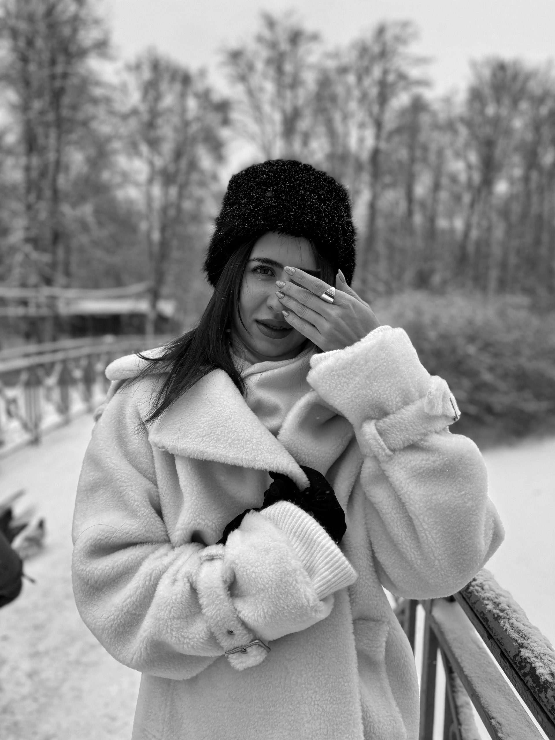 Nahaufnahme: Eine Frau steht im Freien bei Schnee. Sie trägt eine Winterjacke und hält sie vorne mit den Händen geschlossen.