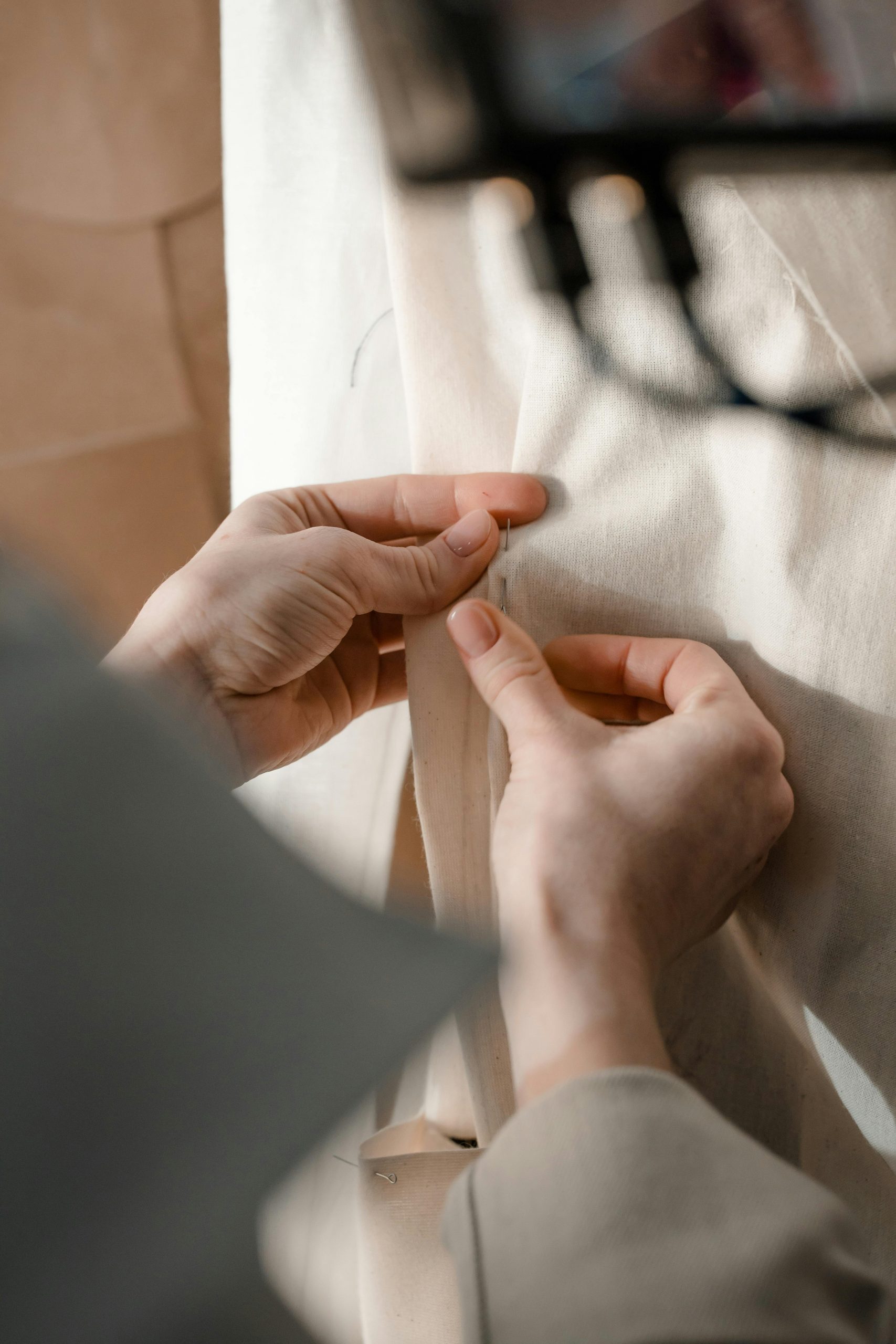 Nahaufnahme: Eine Person arbeitet an einem Textil. Ihre Hände führen ein Stück Faden durch das Textil und näht das Textil.