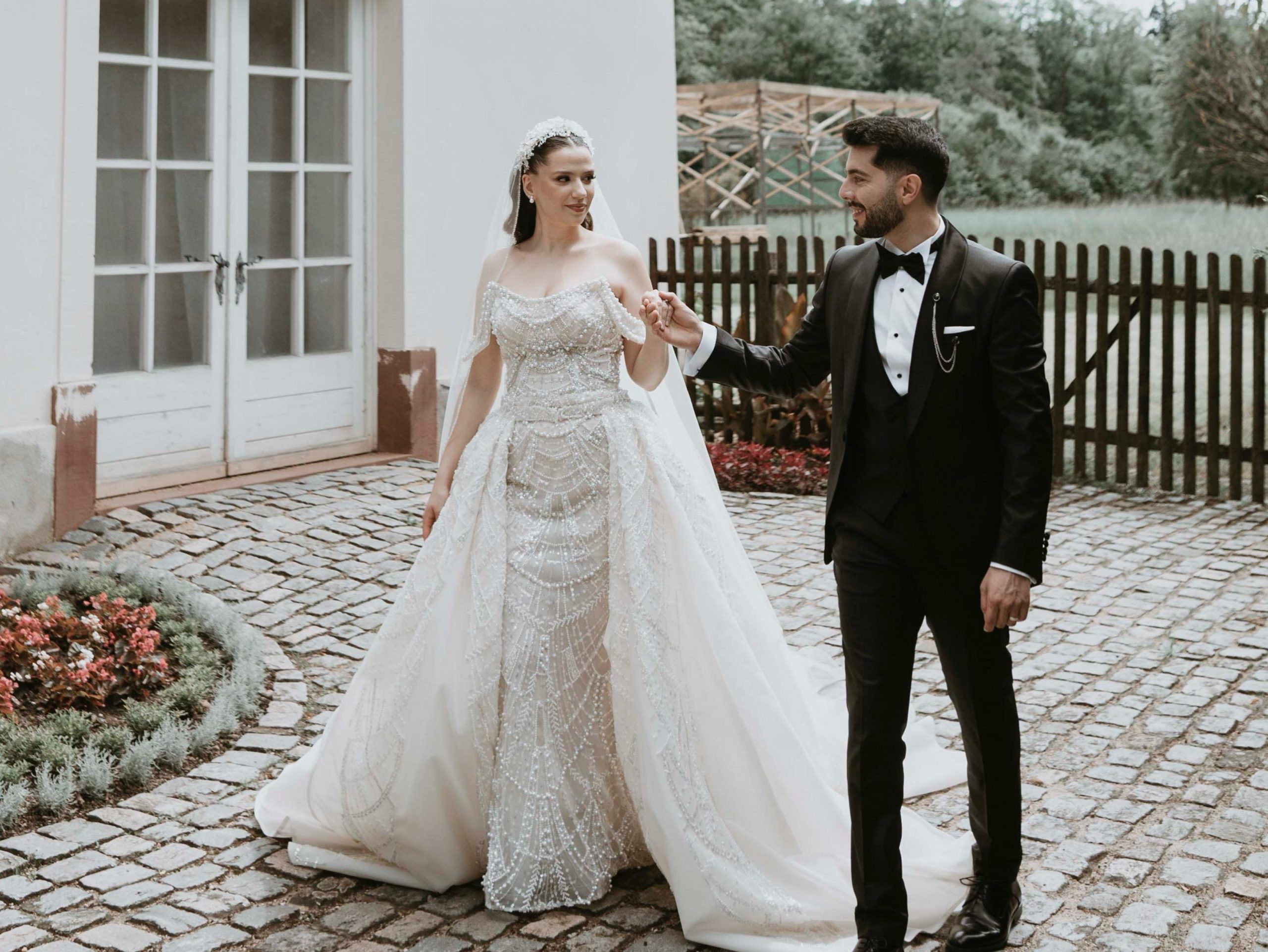 Ein Brautpaar steht im Freien, elegant gekleidet in Abendmode. Die beiden blicken sich an und lächeln einander glücklich an.